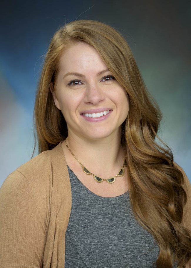 Headshot Image of clinical psychologist Dr. Kimberly Gushanas - a female clinician wearing a gray shirt and brown cardigan