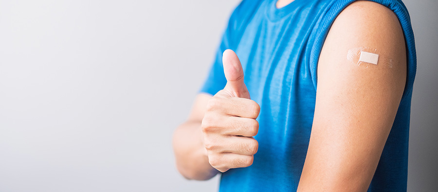 Person wearing a blue sleeveless shirt gives a thumbs‑up, showing a small adhesive bandage on their upper arm after receiving a flu vaccination