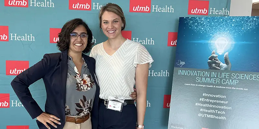 Two women standing next to each other and smiling in front of a UTMB Health backdrop and a sign that reads "Innovation in Life Sciences Summer Camp"