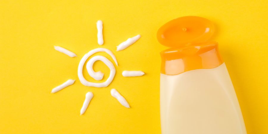 Bottle of sunscreen on a bright yellow background beside white sunscreen arranged in the shape of a sun