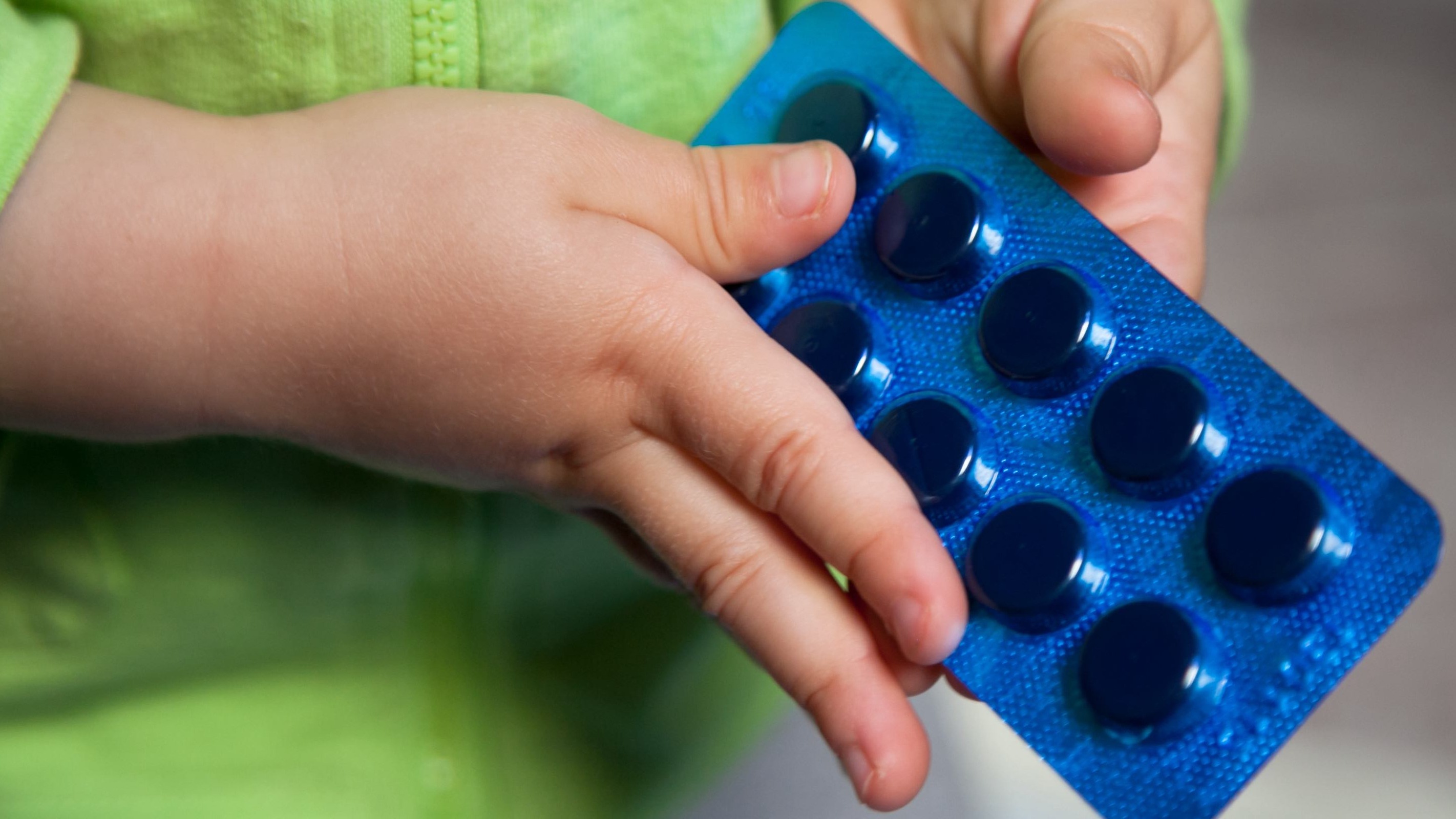 Small hands holding a blue blister pack of pills, highlighting the risk of accidental medication ingestion by young children
