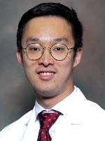 Dr. Charles Wang Professional headshot shows a man wearing glasses, a white coat, and a red patterned tie against a neutral gray background.