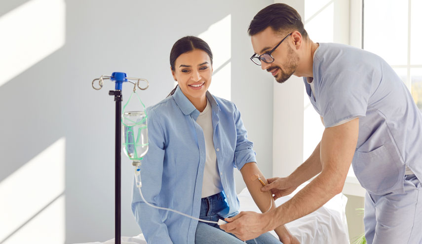 Male nurse helping a female patient receive IV drip fusion or vitamin therapy at UTMB Health