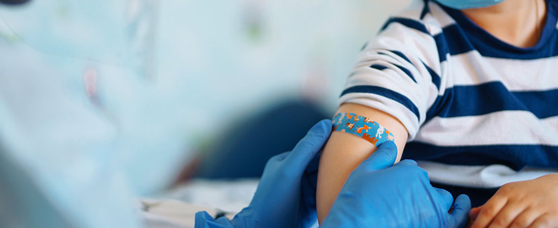 Health care professional wearing gloves places a bandage on a child’s upper arm after a vaccination