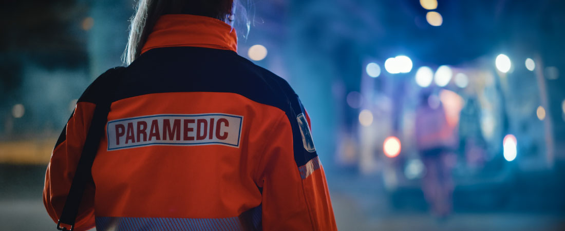 A close up of a paramedic with an emergency scene in the background