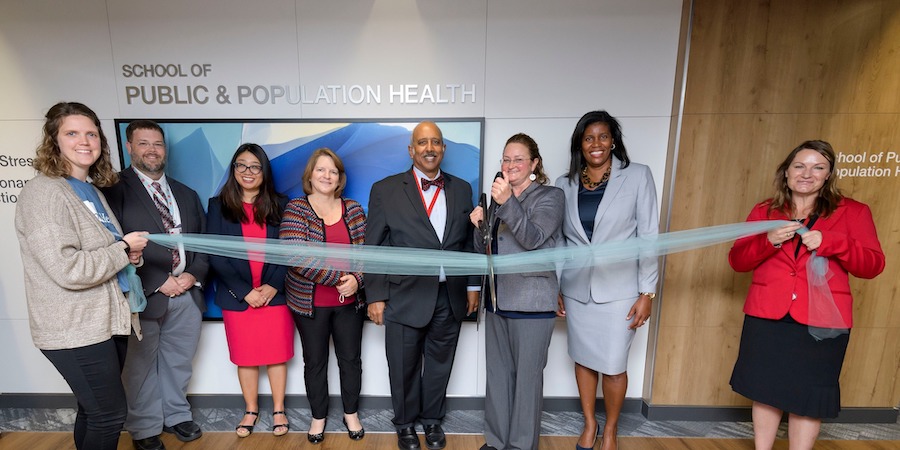 image of individuals holding and cutting ribbon in front of a sign for the UTMB School of Public and Population Health