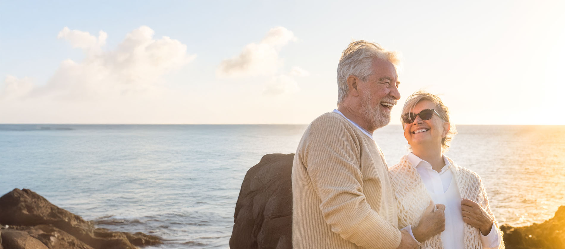close up and portrait of two happy and active seniors or pensioners having fun and enjoying looking at the sunset smiling with the sea - old people outdoors enjoying vacations together.
