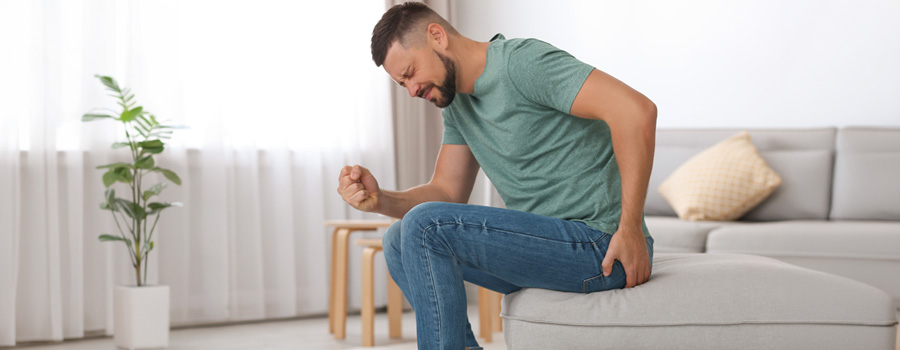 Seated man suffering from hemorrhoid, clenching his fist and touching his butt