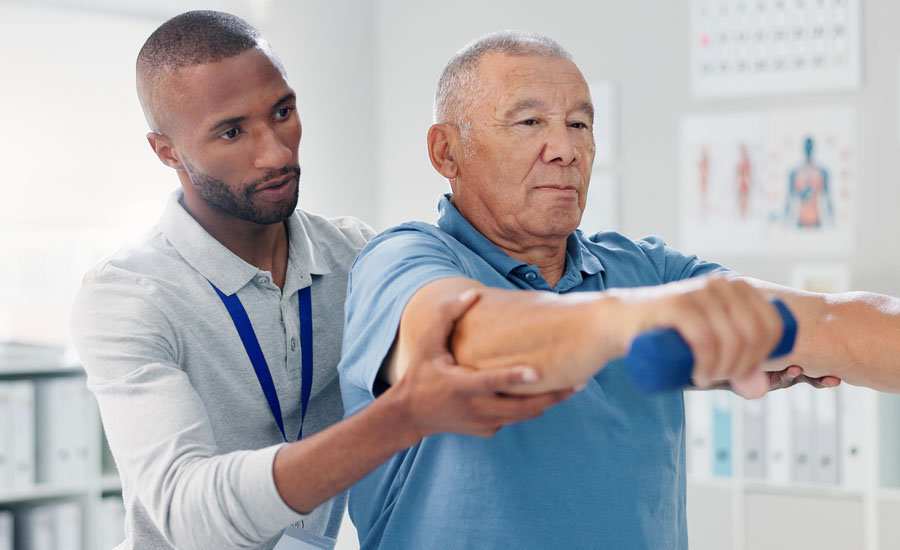 Older man holding weights with assistance from male physiotherapist during physical therapy session