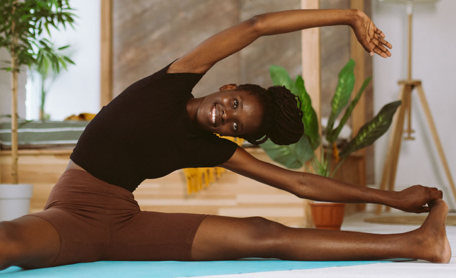 Athletic woman sitting and leaning sideways, touching foot, training on gymnastic mat in decorated studio