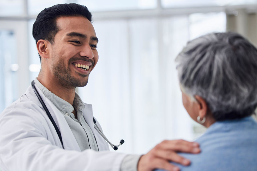 A doctor smiles and rests a hand on an older adult patient’s shoulder during a kidney care visit.