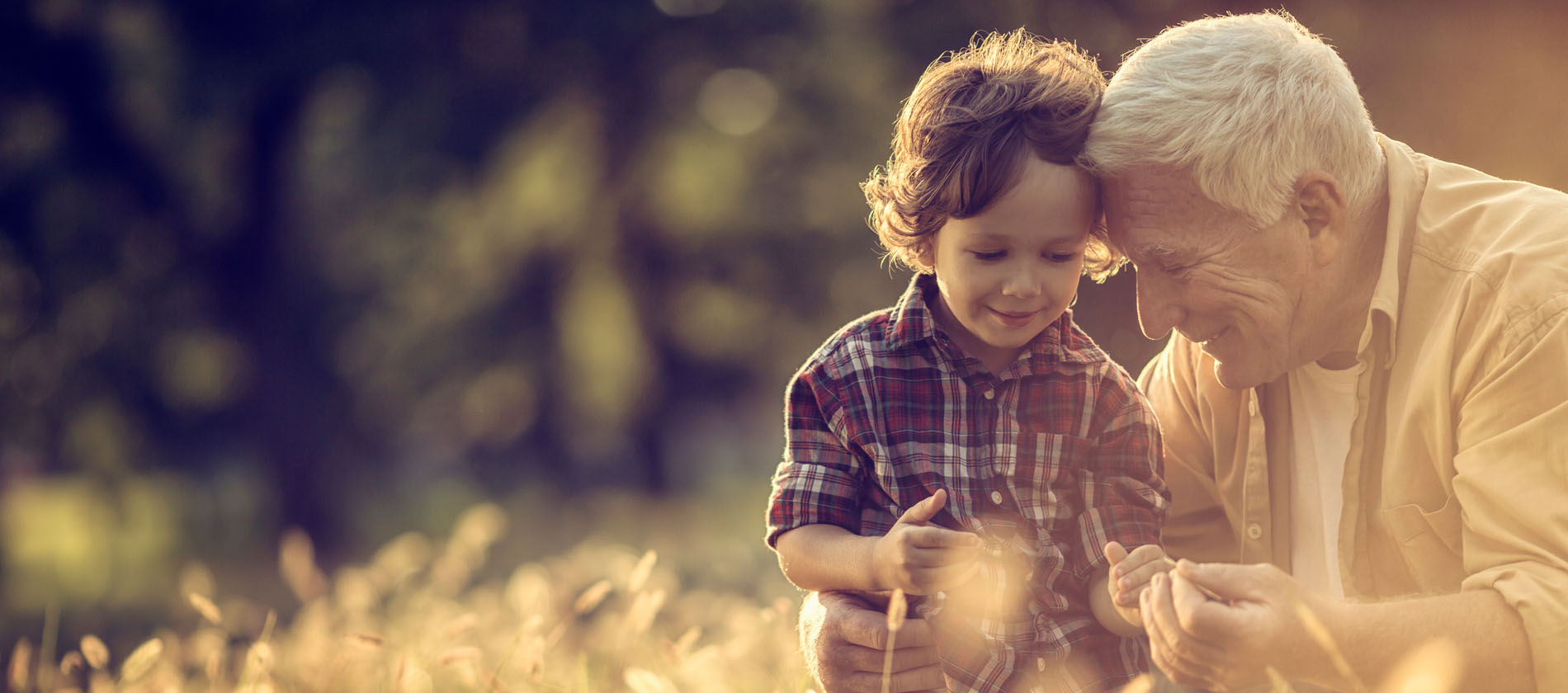 An older adult and young child sit together outdoors smiling and interacting in a peaceful natural setting.