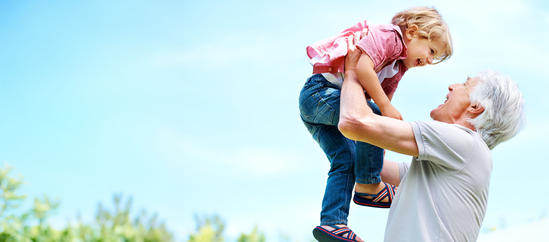 An older adult lifts a child outdoors representing muscle strength balance and daily function with neuromuscular care.