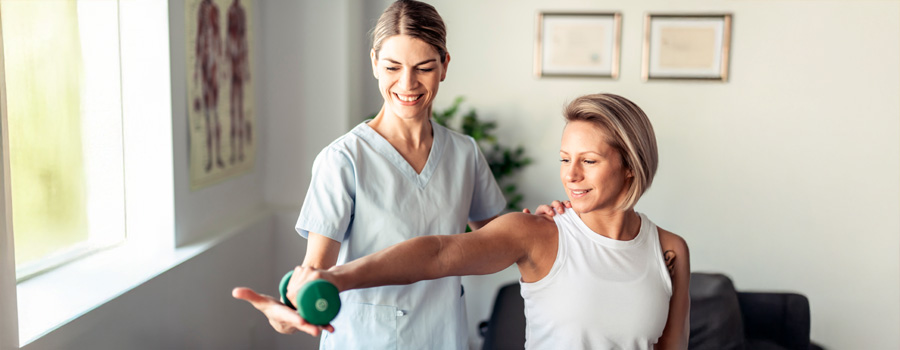 Famel nurse or physical therapist helping female patient holding a dumbbell extend her arm after a shoulder injury at UTMB Health.