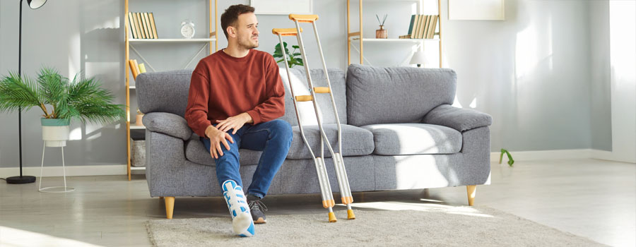 Man sitting on sofa with leg cast on, crutches nearby