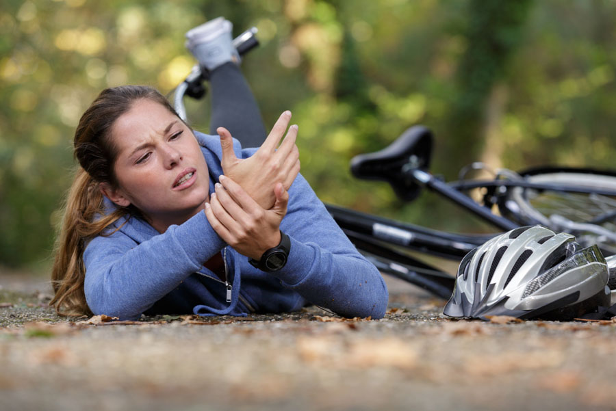Woman lying on ground, holding her wrist in pain, after falling off her bike.