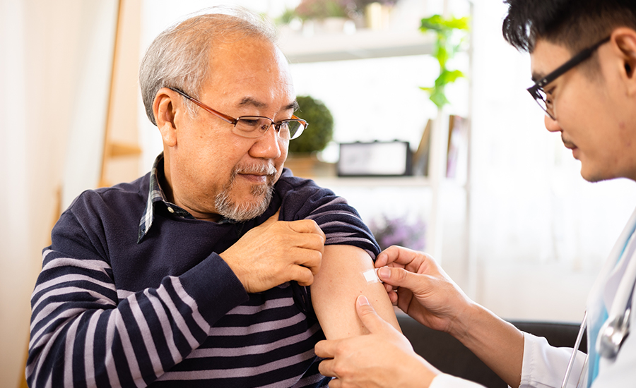 Male doctor placing bandage on elderly male patient’s arm after giving him COVID-19 vaccine