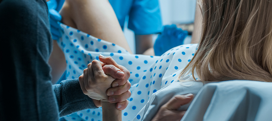 A patient in labor holds a support person’s hand while receiving care from the maternal-fetal medicine team.