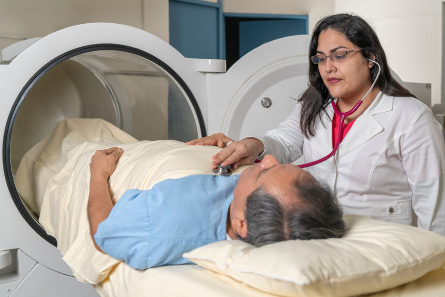 Female doctor placing stethoscope on male patient lying on hyperbaric chamber bed