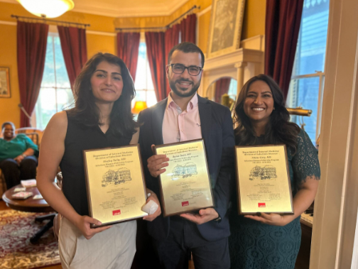 Group of three recent infectious disease graduates holding framed certificates during an indoor recognition event.