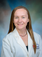 Professional studio portrait of a UTMB Health clinician, Dr. Ewa Tomczak, wearing a white lab coat against a softly blended blue and green background.