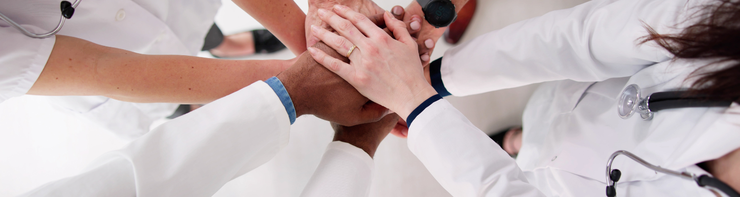 Top view of several doctors standing in a circle showing teamwork by placing hands over hands