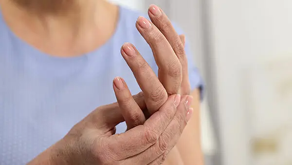 Close-up of a person gently holding their hand while experiencing joint discomfort, illustrating symptoms commonly associated with rheumatologic conditions.
