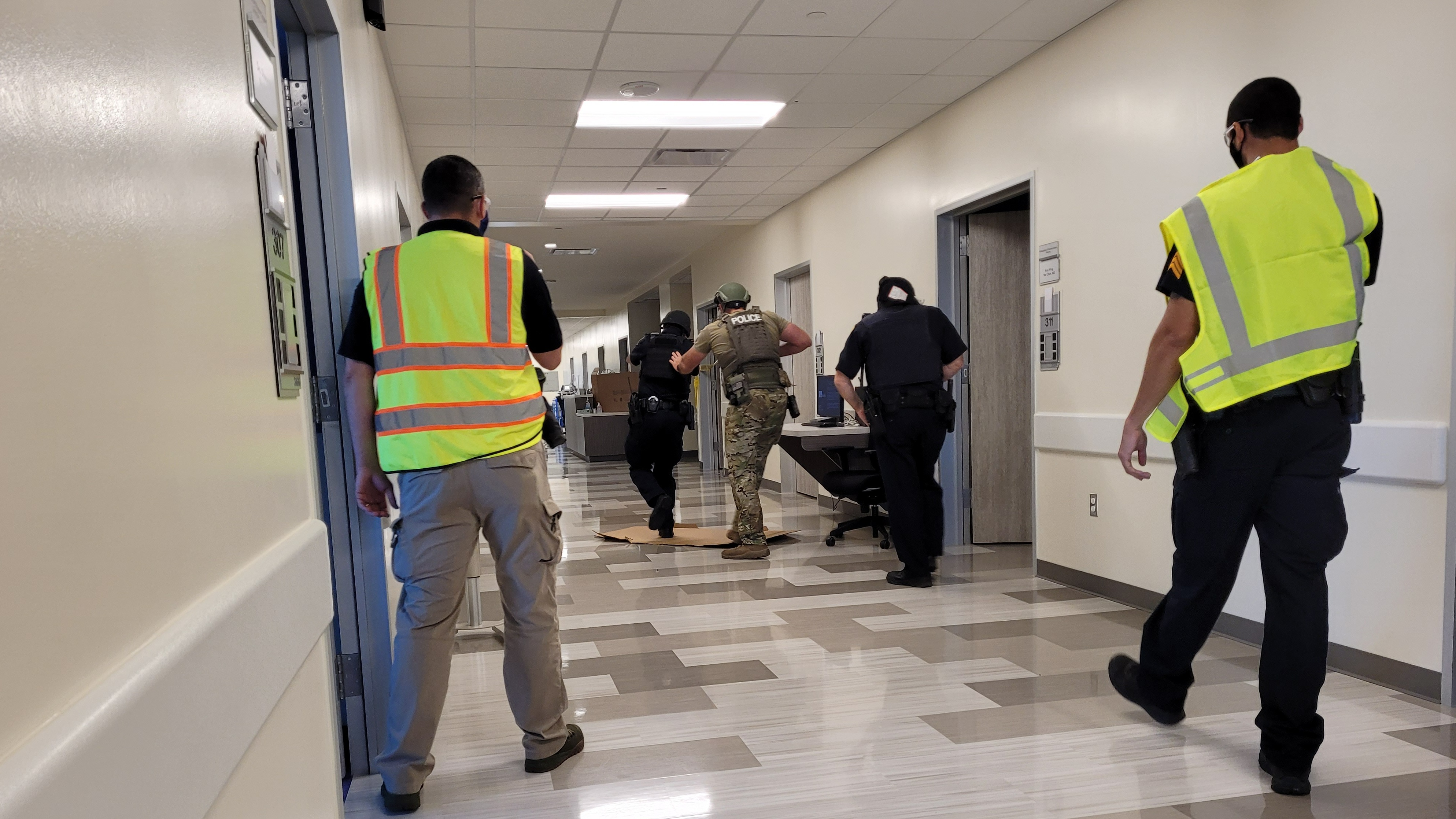 Law enforcement officers and staff in safety vests move down a hospital hallway during a coordinated emergency response drill.