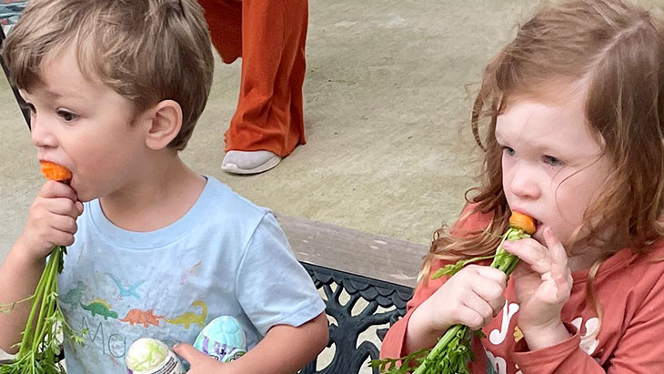 2 kids eating carrot on small bench