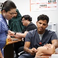 Clinical instructor demonstrates a knee injection technique on a training model while a student observes closely during a hands-on medical skills session.