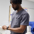 Student standing at a table focusing on assembling or handling a medical instrument during a clinical training session.