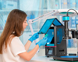 A white woman wiht long hair and a short sleeve white shirt is sitting in front lab equipment and looking at the small turquoise-colored card she is holding.