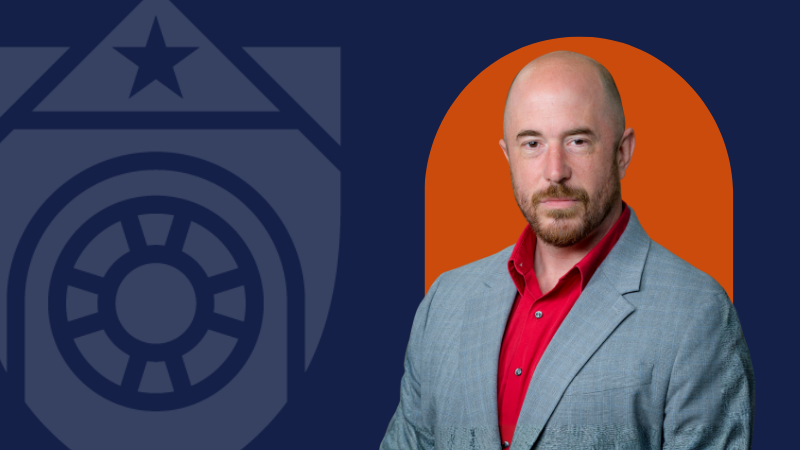 A man in a grey blazer on a navy-blue background with an orange backdrop directly behind him and the UTMB logo to the left