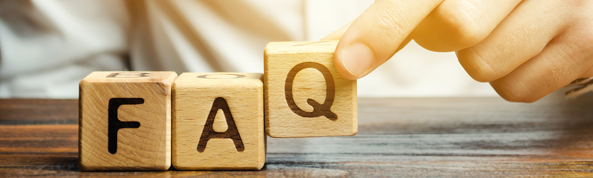 A hand placing a wooden block with the letter “Q” next to blocks labeled “F” and “A,” forming the word “FAQ.”