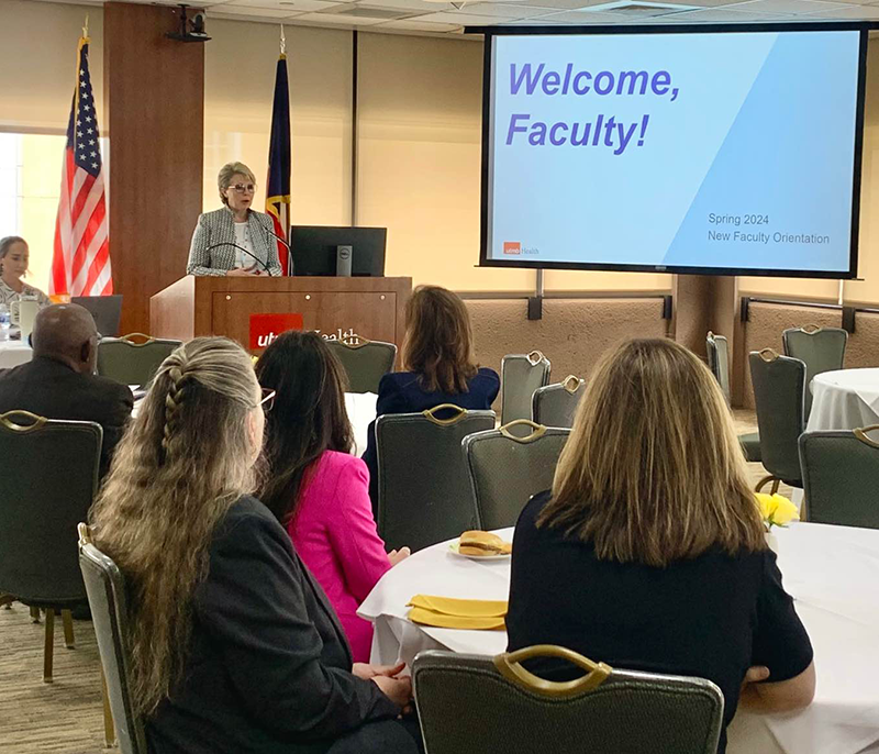 Dr. Chubinskaya behind the podium in front of a crowd with a presenter screen to the right that features "Welcome, Faculty" on it.
