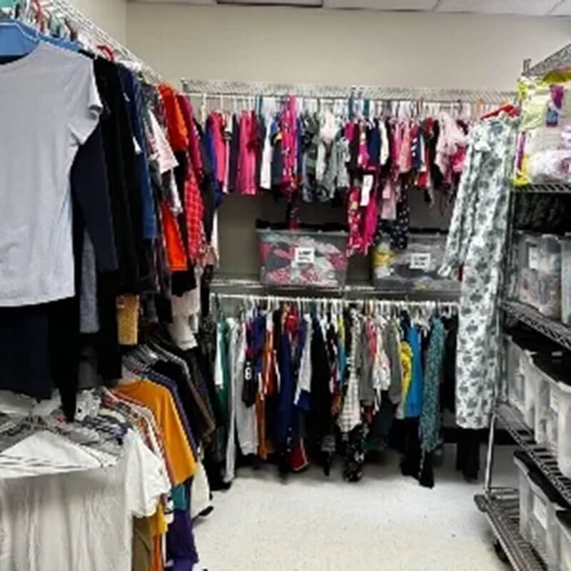 Hospital closet full of clothing donations on clothes racks and in boxes on metal shelves.