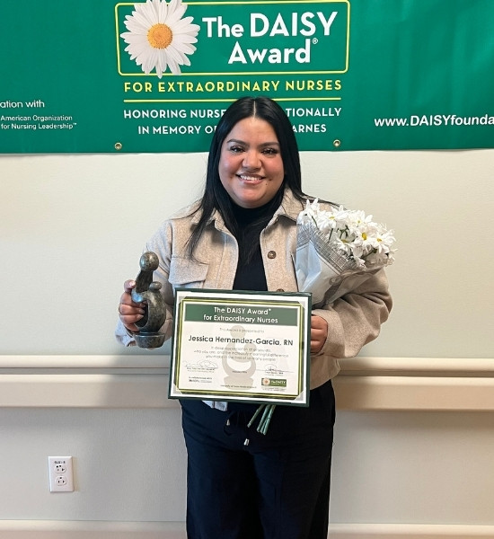 Jessica Hernandez-Garcia, RN, stands smiling with her DAISY certificate and award.