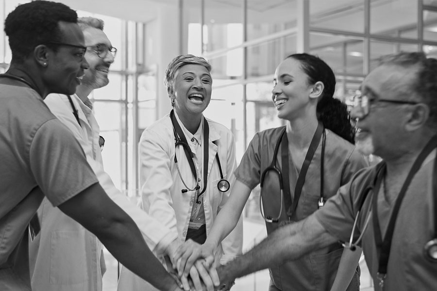 Smiling multiracial doctors placing hands together for huddle in hospital meeting. Proud health care worker community for medical mission achievement.