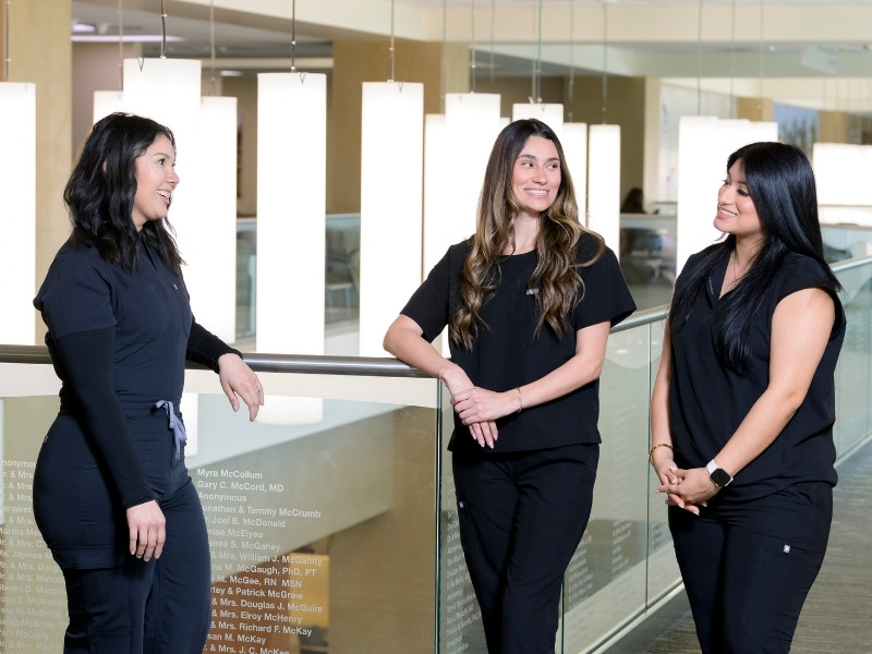Three nurses in black scrubs talk together on the fourth floor of Jennie Sealy Hospital.