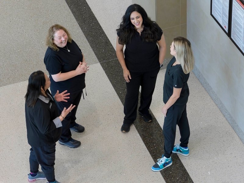 Four nurses in black scrubs talk to each other in Jennie Sealy Hospital.