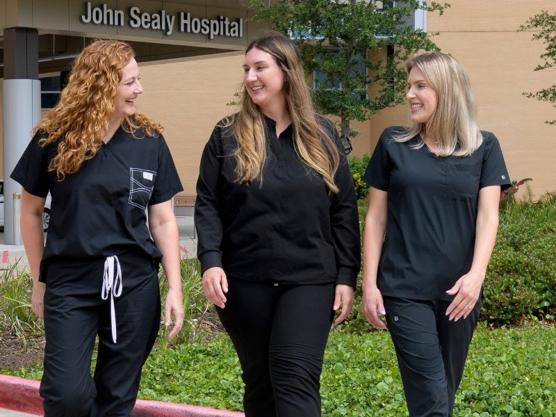 Three nurses in black scrubs talk in front of John Sealy Hospital.