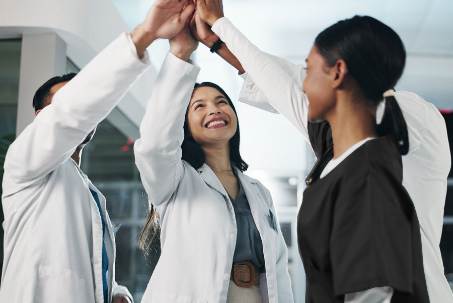 Smiling multiracial health care team giving group high five in hospital for success. Doctors and nurses celebrating in hospital lobby.