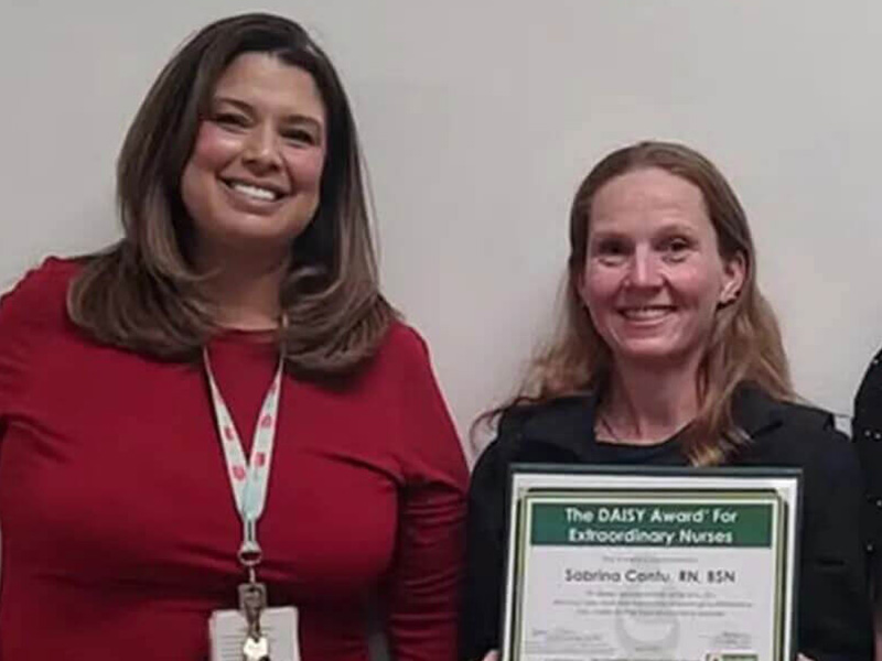 DAISY Award recipient, Sabrina Cantu, smiles holding her certificate next to a colleague.