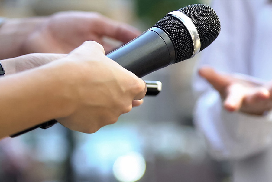 Reporters holding microphones and taking notes during an interview