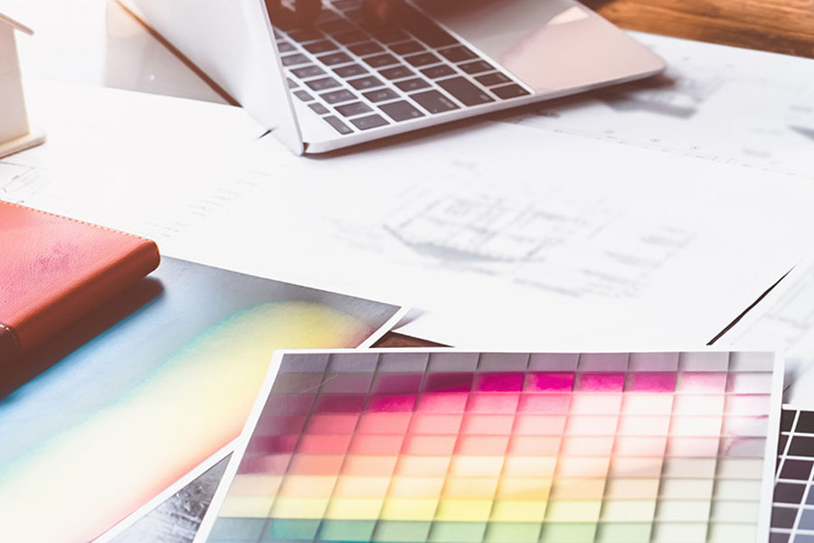 A designer choosing colors from a swatch book while working on a laptop