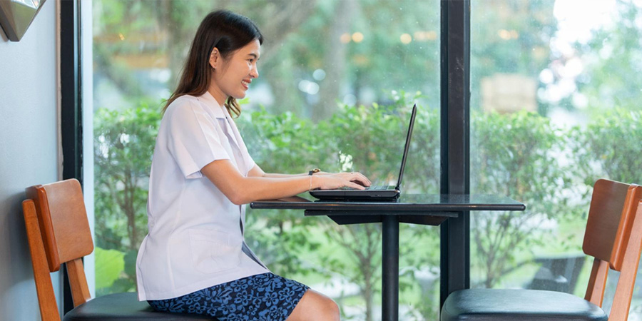 A smiling woman sitting at a table typing on a laptop.