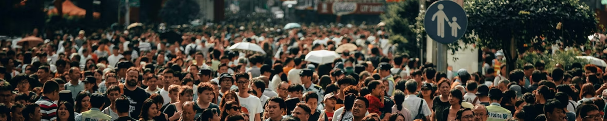 A large crowd of people walking through a busy city street, representing population-level health and public health in community settings.