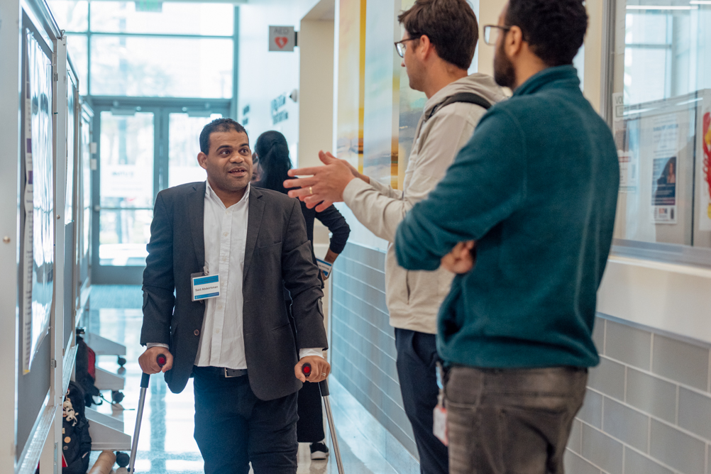 A presenter speaks with attendees in the hallway during the poster session at the UTMB Public Health Symposium.