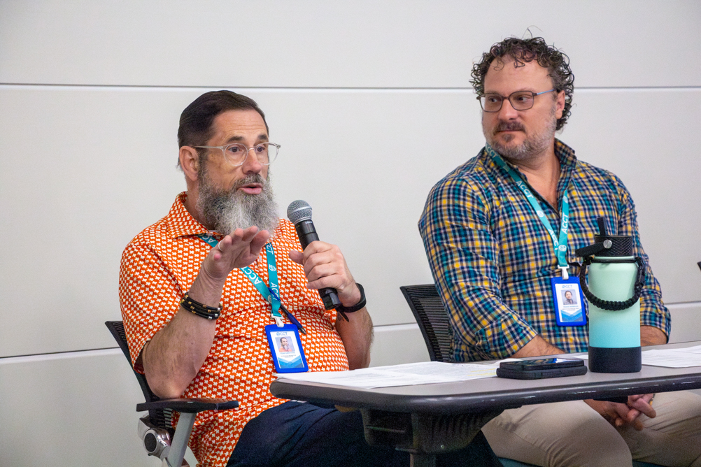 Two Community Voices Panel participants sit at a table during UTMB’s National Public Health Week event as one speaks into a handheld microphone and the other listens.