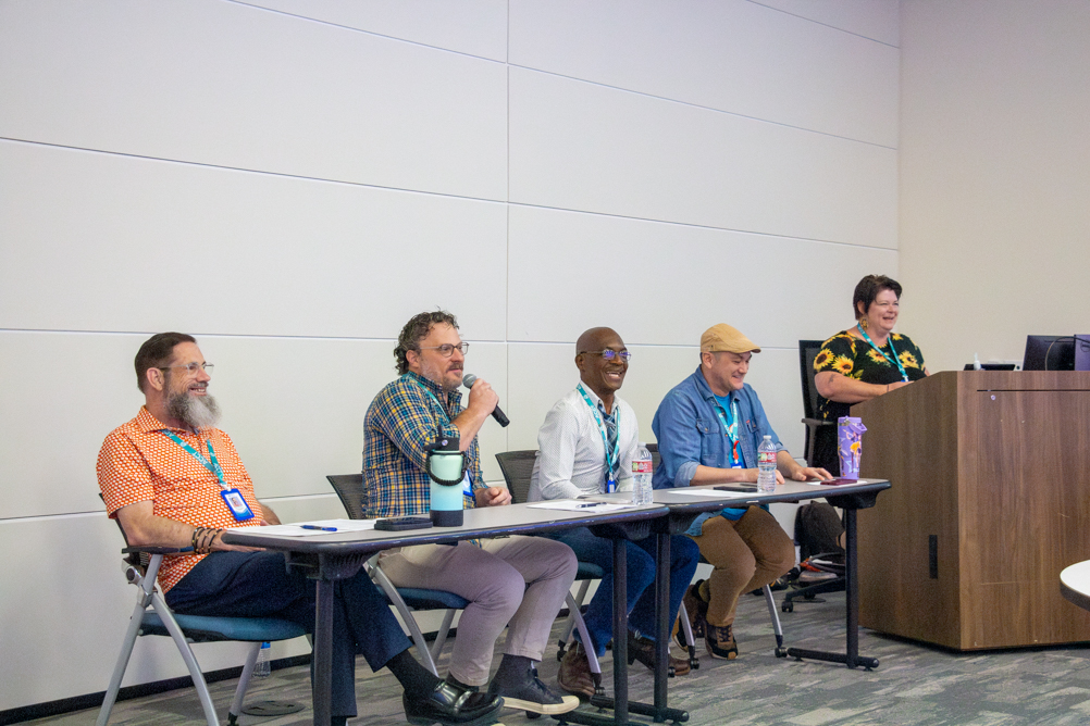 Five speakers from Access Care of Coastal Texas take part in the Community Voices Panel at UTMB, with four seated at the front of the room and one seated at the lectern.